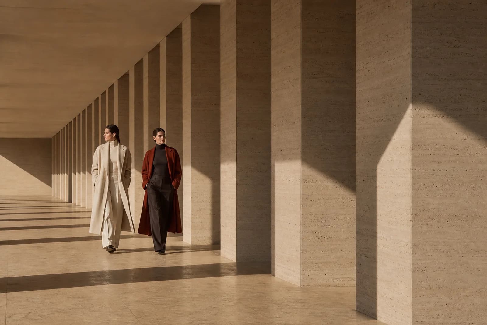 Two models wearing Orra tailoring in a sunlit stone colonnade